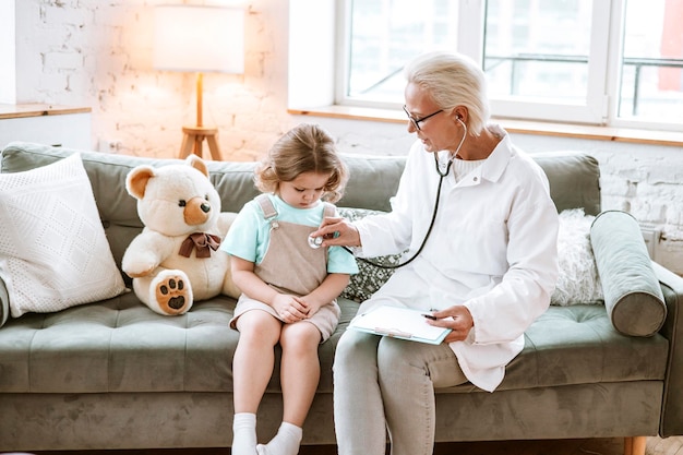 cute little curly haired girl plays doctor with a stethoscope and treats and cares a teddy bear