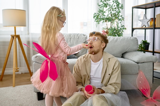 Cute little daughter feeding father wearing funny festive outfit, game time at home on weekend