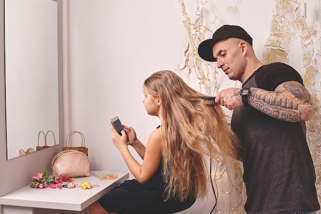 Cute little daughter and her tattoed dad are playing together near a mirror dad is doing his daughte...