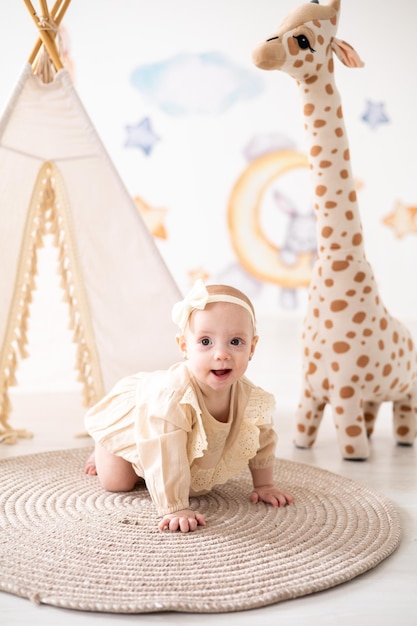 A cute little European girl with brown eyes in a beige bodysuit made of natural fabric plays in the children's room at home against the background of a wigwam and plush toys