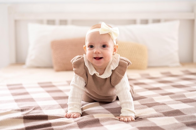 ベージュのニットスーツを着た茶色の目をしたかわいいヨーロッパの女の子が、自宅のベッドを這い、ホームテキスタイルをほほ笑む