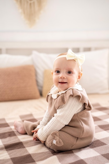 ベージュのニット スーツを着た茶色の目をしたかわいい小さなヨーロッパの女の子が自宅のベッドに座ってホーム テキスタイルに笑みを浮かべて