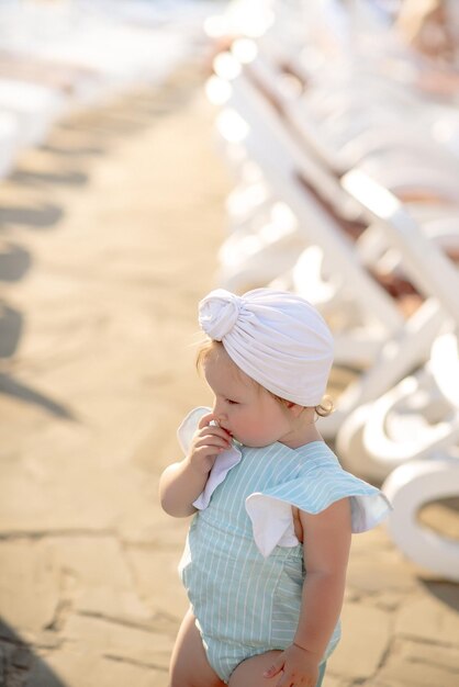 Bambina sveglia di 1 anno sulla spiaggia del resort in estate in un vestito alla moda