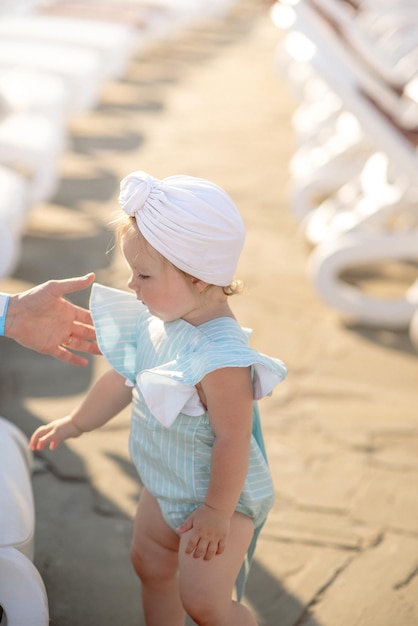 Cute little girl 1 year old on the beach at the resort in summer in a trendy outfit