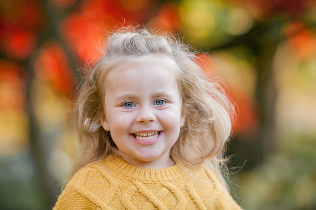 Cute little girl of 3 years old in a knitted sweater walks in an autumn bright park Portrait of a happy child Fall