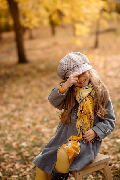 Cute little girl 5 years old with curly hair laughs, playing with fallen leaves in autumn