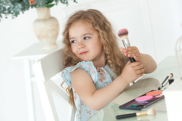 Cute little girl applying make up looking into mirror. Little fashionista girl playing with her mother`s cosmetics. Adorable child indoors