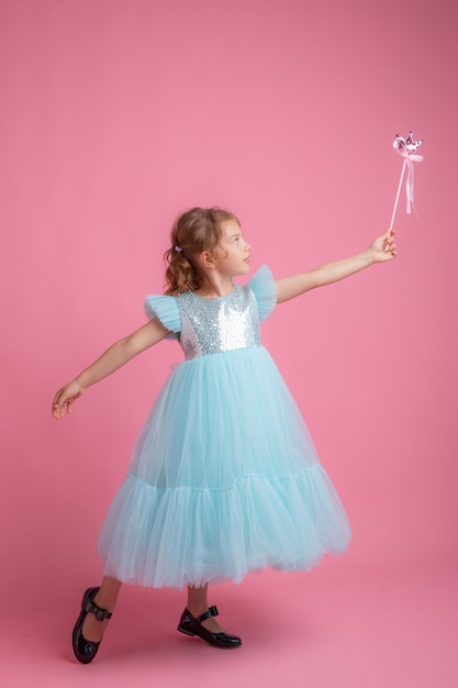Cute little girl in a beautiful dress holding a fairy magic wand on a pink background