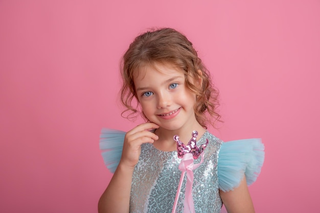 Cute little girl in a beautiful dress holding a fairy magic wand on a pink background