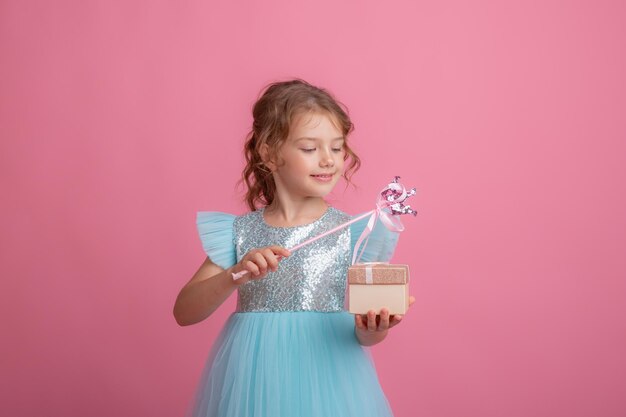 ピンクの背景に美しいドレスを着たかわいい女の子が妖精の魔法の杖と贈り物を持っている
