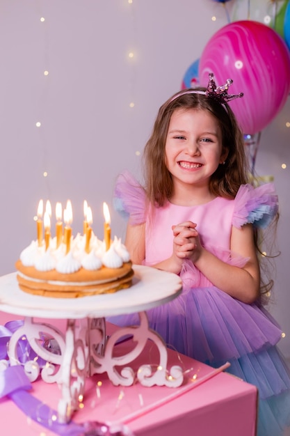 Foto bambina carina in un bel vestito esprime un desiderio e spegne le candeline sulla torta di compleanno