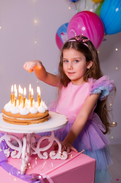 Cute little girl in a beautiful dress makes a wish and blows out the candles on the birthday cake