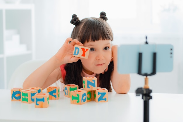 Cute little girl blogger playing with wooden colorful cubes with letters and showing them online