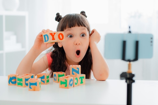 귀여운 소녀 블로거가 나무로 된 다채로운 큐브를 글자로 가지고 놀고 온라인으로 보여줍니다.