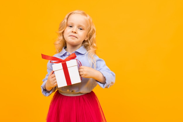 La bionda sveglia della bambina tiene il contenitore di regalo su un giallo