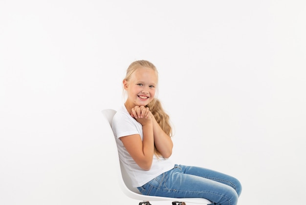 Cute little girl blonde sits on a chair on a white background