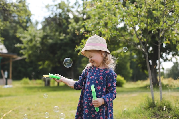 Cute little girl blowing soap bubbles on a walk in summer outdoors