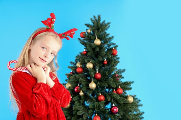 Cute little girl on blue background with Christmas tree