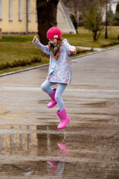 A cute little girl in a blue cape pink boots and a pink hat
runs through puddles and has a fun