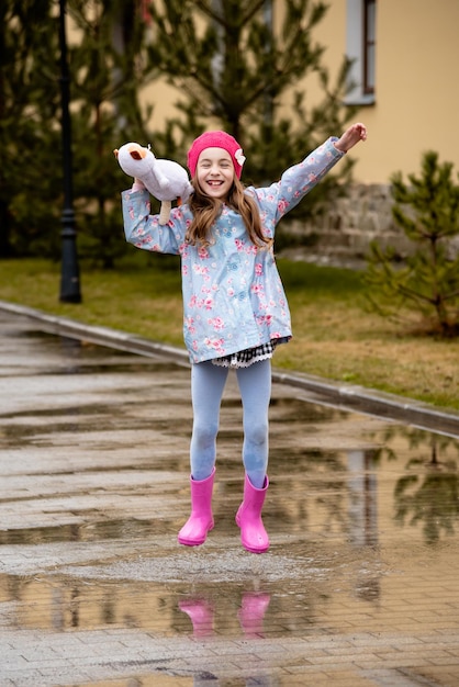 A cute little girl in a blue cape pink boots and a pink hat
runs through puddles and has a fun