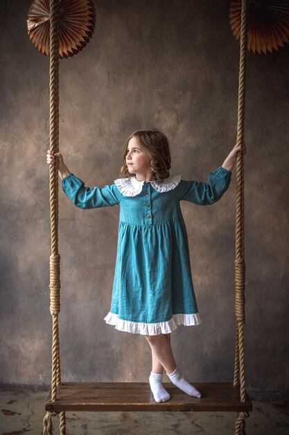 Cute little girl in a blue dress on a swing