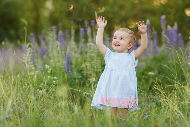 Cute little girl in blue dress try to catch butterfly