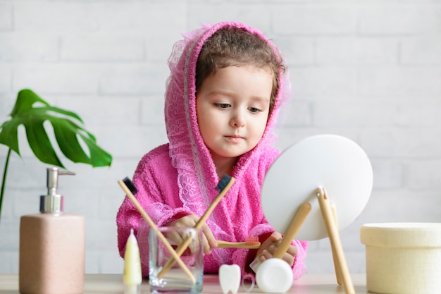 Cute little girl brushing teeth, washing face in bathroom, looking at the mirror. daily self care of the child.