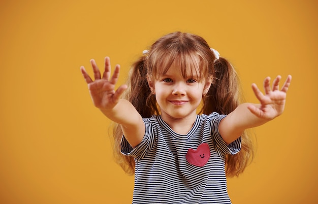 Photo cute little girl in casual clothes in the studio against yellow background.