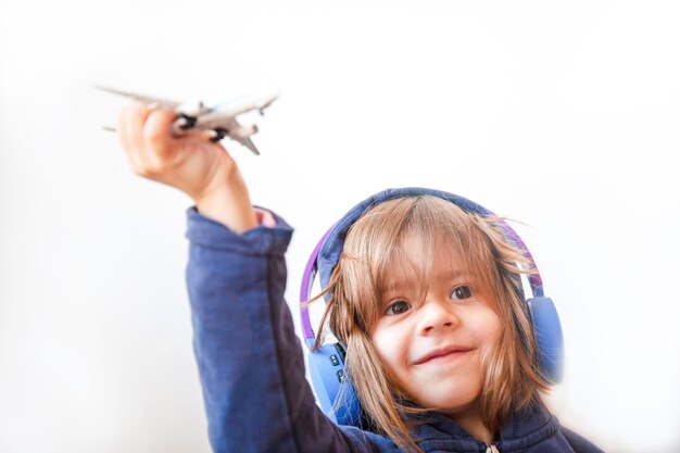 Bambina sveglia in felpa casual che ascolta la musica con le cuffie senza fili e gioca con l'aeroplano giocattolo luce diffusa naturale tema dell'infanzia concetti di viaggio e di sogno