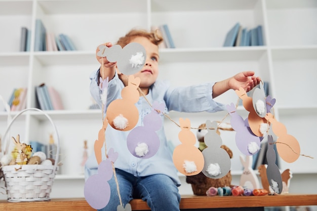 Photo cute little girl celebrating easter holidays indoors and holding paper bunnies in hands