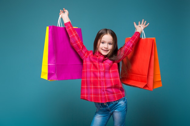 Cute little girl in checkered shirt with brunet hair hold different bags