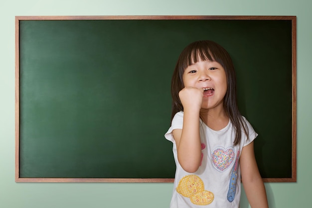 Cute little girl cheering on a background of black school\
board