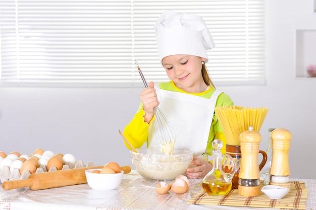 Cute little girl in chef's hat baking cake in the kitchen