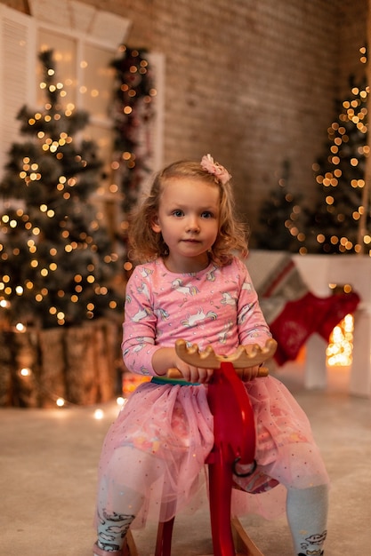 Cute little girl child in a fashionable pink dress sits on a red toy moose