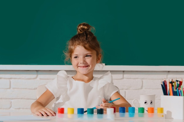 Cute little girl child painting with paints color and brush cute school girl drawing in class at sch