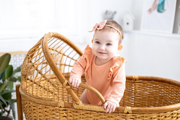 A cute little girl child in a pink bodysuit is standing in a wicker cradle at home looking at the camera smiling children's healthy sleep