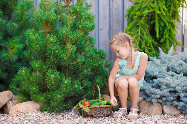 Cute little girl collects crop cucumbers and tomatos in greenhouse