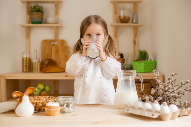 Cute little girl in a cotton dress at home in a wooden kitchen prepares an Easter cake