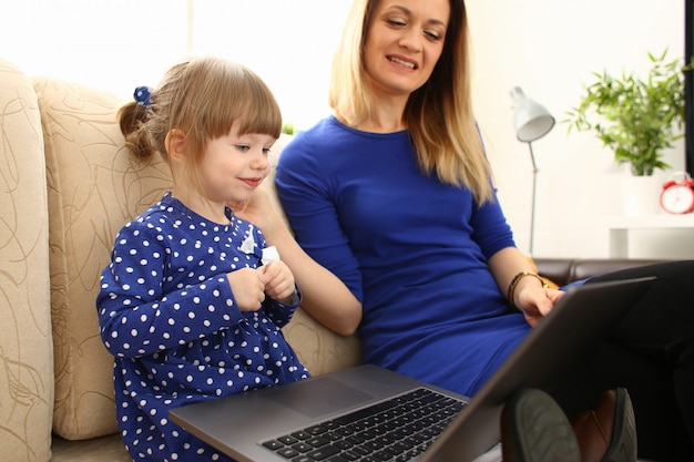 Cute little girl on couch with mom use laptop