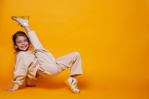 Cute little girl dancing on a yellow wall Space for text