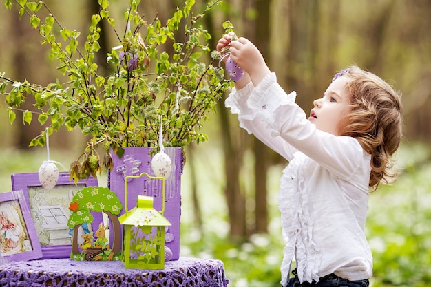 Cute little girl decorating branches with Easter eggs. Springtime in the garden