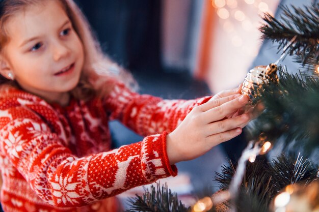 Cute little girl decorating christmas tree indoors at new year holidays.