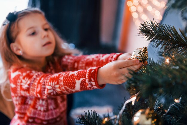 Photo cute little girl decorating christmas tree indoors at new year holidays.