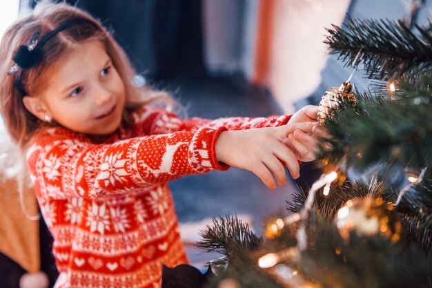 Cute little girl decorating christmas tree indoors at new year holidays.