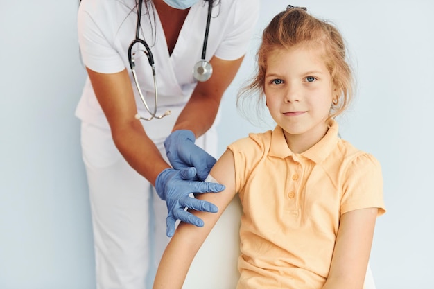 Photo cute little girl doctor in uniform making vaccination to the patient