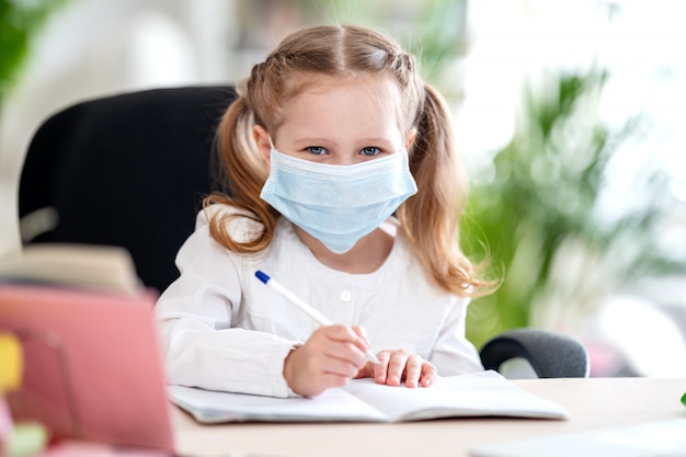 Cute little girl, doing homework, writing in notebook, using laptop, e-learning