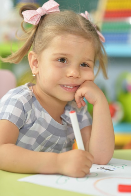 Bambina sveglia che disegna con il pennarello mentre è seduto al tavolo nella sua stanza