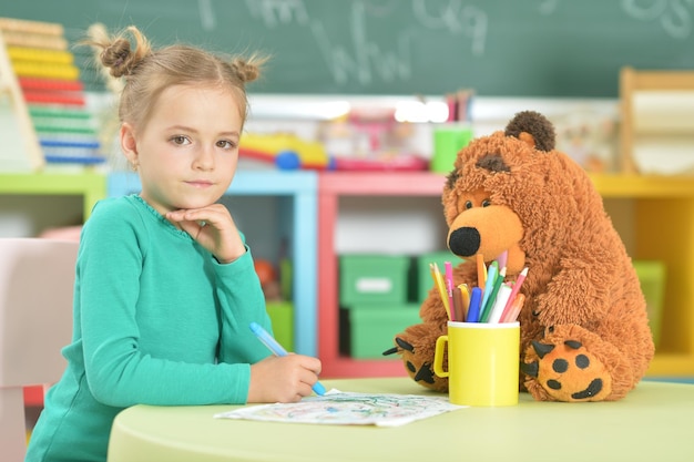 Cute little girl drawing with felt pen while sitting at table in her room