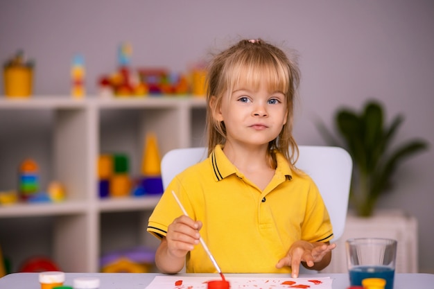 Cute little girl draws with paints in kindergarten