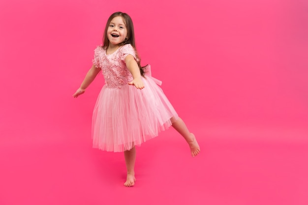 Cute little girl dreams of becoming a ballerina. Little Dancing Girl. Studio Shoot Over Pink Background.